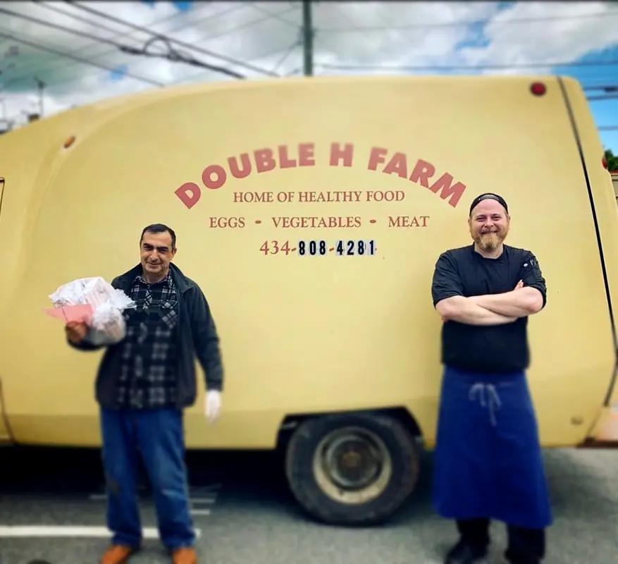 The farm's cream trailer, lettered Double H Farm, Home of Healthy Food, with Ara and a chef beside it